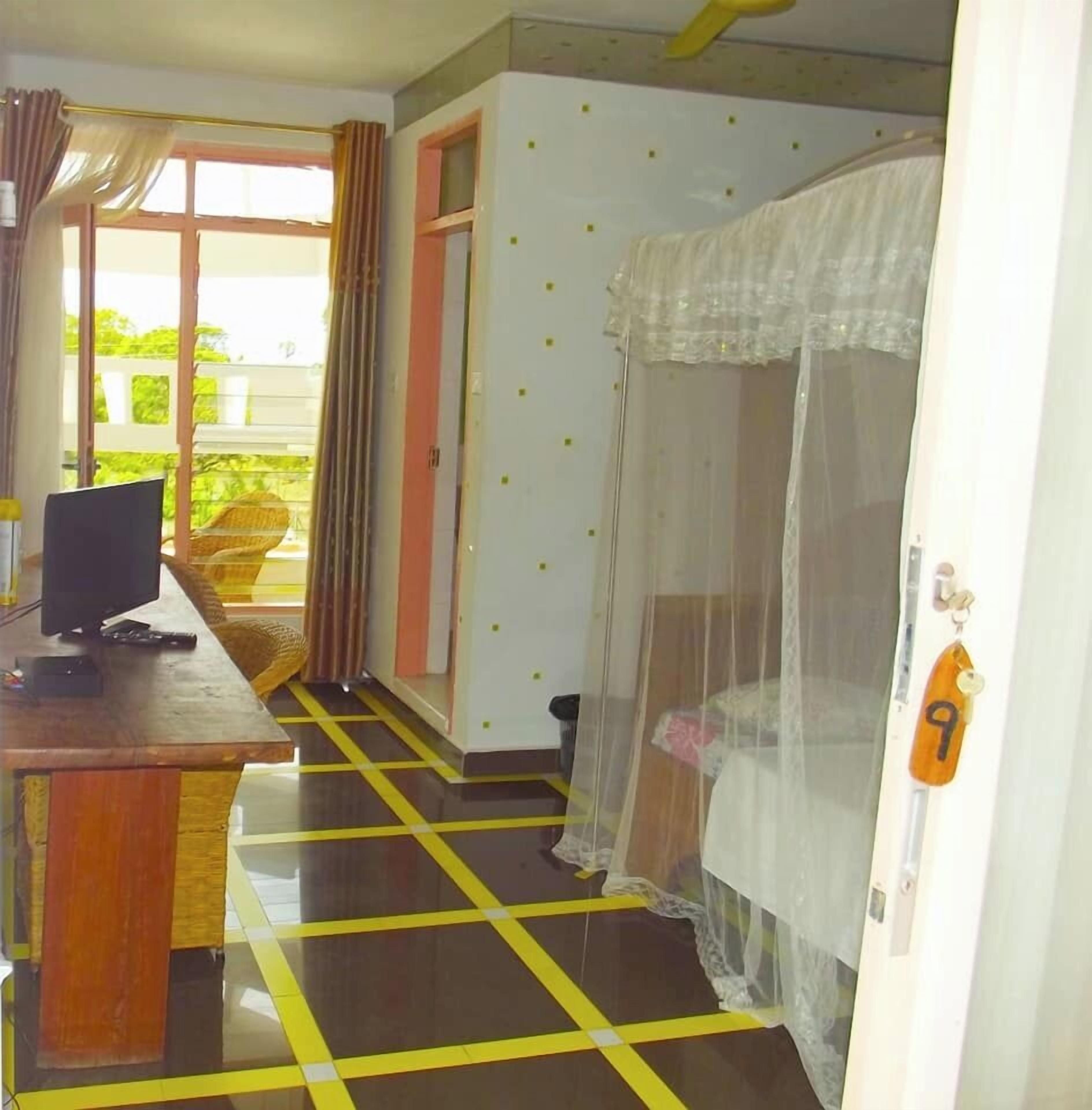 Quarto com cama, escrivaninha com computador, janela com cortinas e porta com número.
