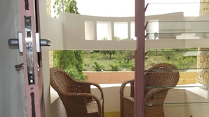 A balcony with wicker furniture, a view of greenery, and a stone wall.