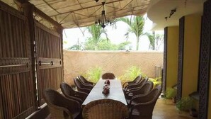 An outdoor dining area with wicker chairs and a long table, surrounded by a high wall with a textured pattern.