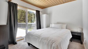 Ein Schlafzimmer mit Bett, Nachttisch, Lampe, Kleiderschrank und Blick ins Freie.