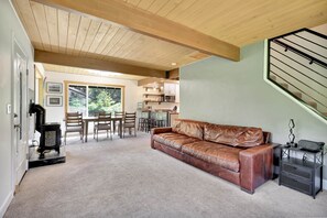 Ein gemütliches Wohnzimmer mit braunem Ledersofa, einem Essbereich mit Holzsesseln, einer Küche im Hintergrund und einer Treppe.