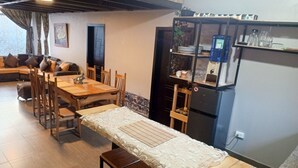 A dining area with a wooden table and chairs, a bench, a refrigerator, and a shelf with kitchenware.