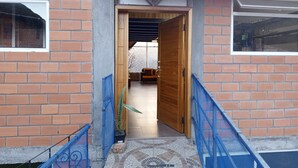 A brick building with a wooden door, a blue metal railing, and a patterned floor.