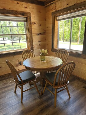 A wooden interior with a round table and chairs, large windows with a view of trees, and a wooden floor. - Cozy 2-bedroom house in Nancy, 2 Miles From Wolf Creek Marina! Plenty of parking (Nancy)