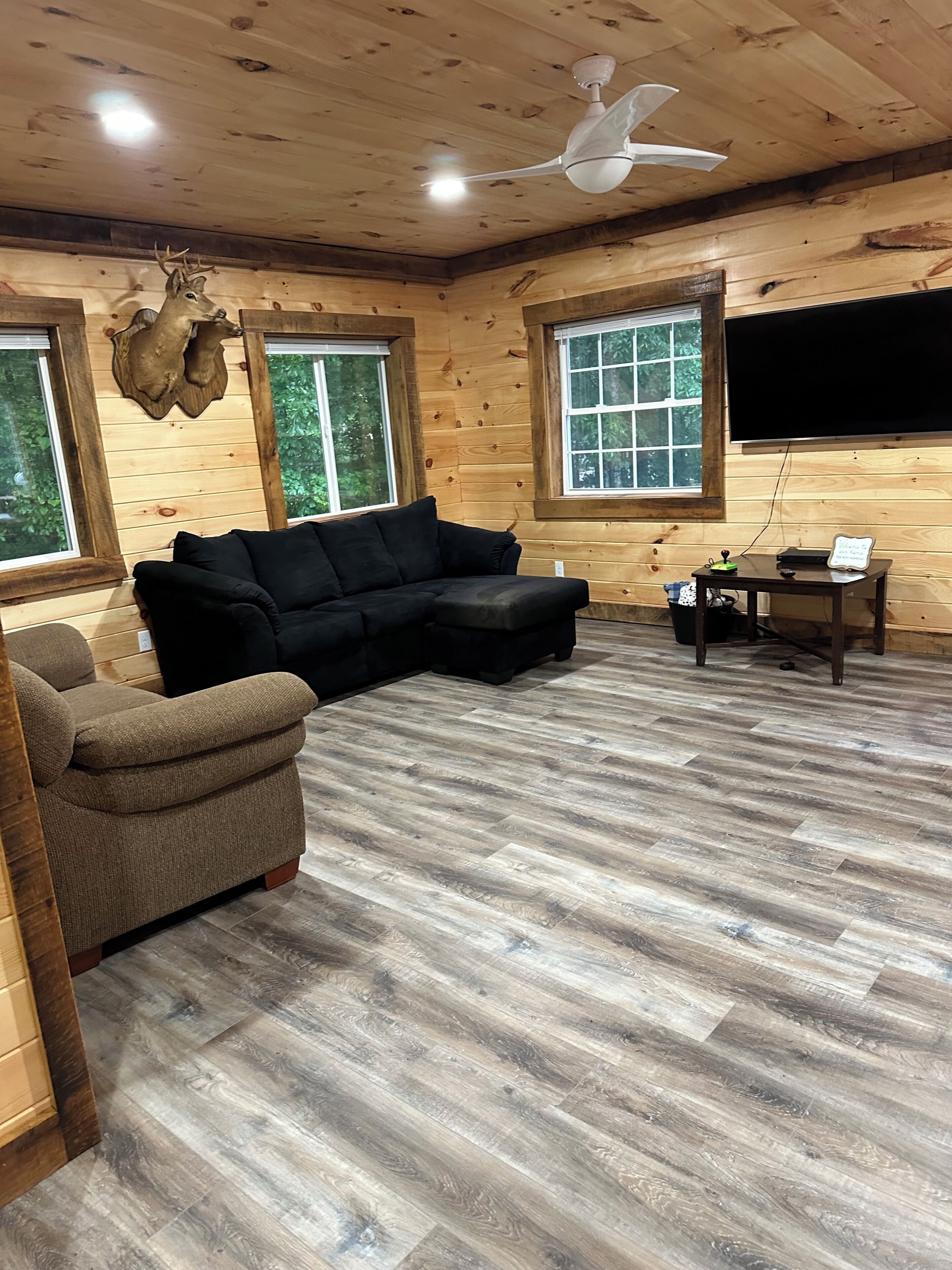 A wooden interior with a sectional sofa, a television, and a ceiling fan.
