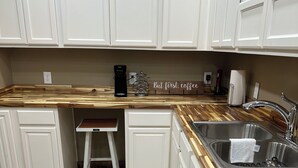Eine Küche mit weißen Schränken, einer Holz Arbeitsplatte, einer Edelstahl-Spüle, einer Kaffeemaschine und einem Handtuchhalter.