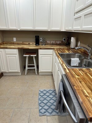 A kitchen with white cabinets, a wooden countertop, a stainless steel sink, a coffee maker, and a towel rack. - Cozy 2-bedroom house in Nancy, 2 Miles From Wolf Creek Marina! Plenty of parking (Nancy)