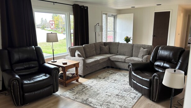 A living room with a sectional sofa, two leather armchairs, a small wooden table, and a floor lamp. - Enjoyable 3-bedroom house in charming Rogers City perfect for relaxing (Rogers City)