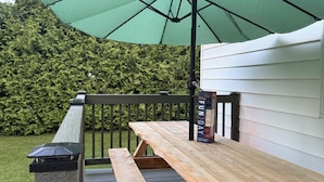 A wooden picnic table with benches, a green umbrella, and a metal railing on a wooden deck. - Enjoyable 3-bedroom house in charming Rogers City perfect for relaxing (Rogers City)