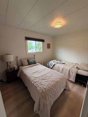 Ett sovrum med två sängar, ett fönster, en taklampa och ett nattduksbord med en lampa.