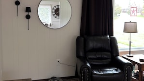 A room with a leather chair, a round mirror, and two wall-mounted lamps. - Enjoyable 3-bedroom house in charming Rogers City perfect for relaxing (Rogers City)
