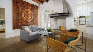 Een gezellige woonkamer met een bank, stoelen, een salontafel, een groot houten sculptuur en een witte deur.
