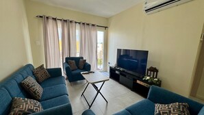 A living room with a sofa set, a coffee table, a TV, and an air conditioning unit. - Gated Luxury Fort George Retreat | Panoramic Port-of-Spain Views | Sleeps 8+ (Port of Spain)