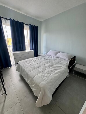 Un dormitorio con cama, mesita de noche, cómoda y ventana con cortinas.