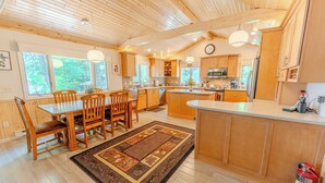 A spacious kitchen with wooden cabinets, a dining area with a table and chairs, and large windows. - Straits Chilling: Sleeps 6*Pet Included*Hot Tub*Kayaks*Paddle Boat! (Wetmore)