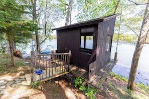 A wooden cabin with a dock, surrounded by trees and a lake.