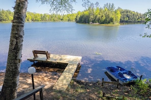 A wooden dock extending into a calm lake, surrounded by trees and a clear sky.