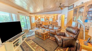 A spacious living room with a large flat-screen TV, leather sofas, a coffee table, and a patterned rug. - Straits Chilling: Sleeps 6*Pet Included*Hot Tub*Kayaks*Paddle Boat! (Wetmore)