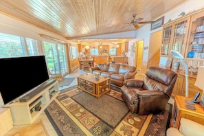 A spacious living room with a large flat-screen TV, leather sofas, a coffee table, and a patterned rug.