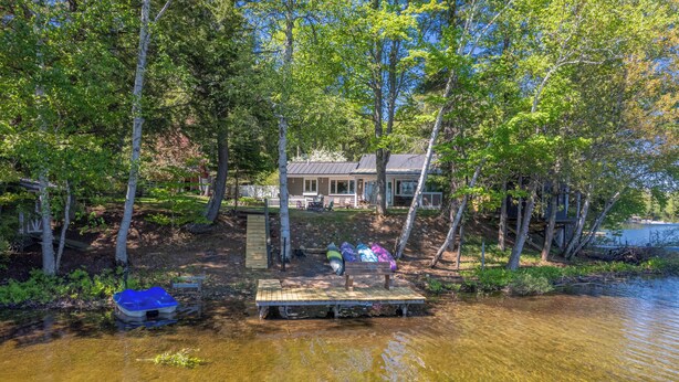 A lakeside cabin with a dock, surrounded by trees and a clear view of the water. - Straits Chilling: Sleeps 6*Pet Included*Hot Tub*Kayaks*Paddle Boat! (Wetmore)