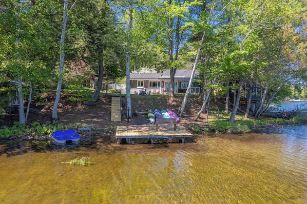 A lakeside cabin with a dock, surrounded by trees and a clear view of the water.