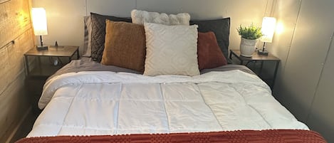 Una cama con ropa de cama blanca, un plaid rojo y tres cuadros en la pared.