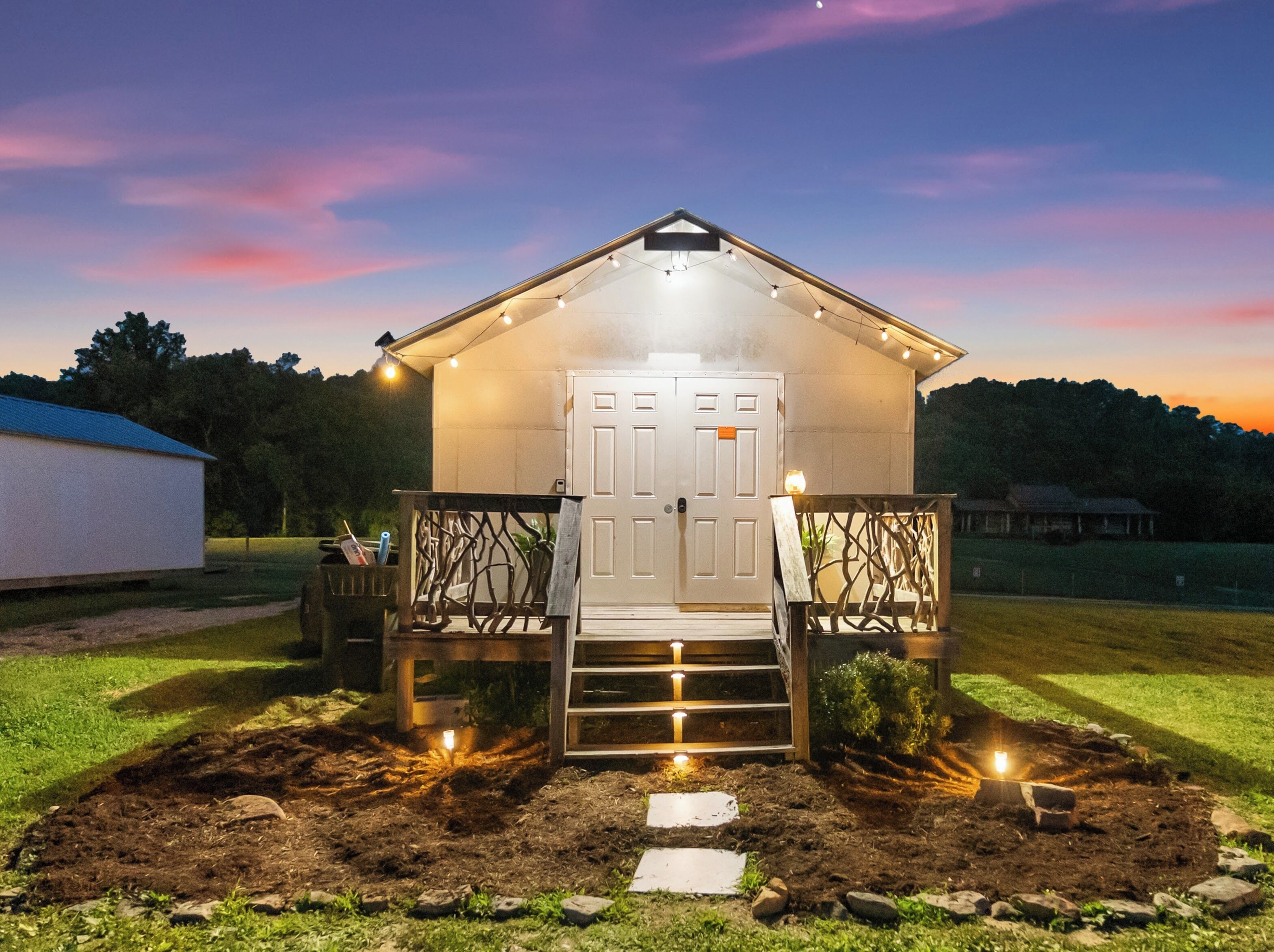 A small, illuminated structure with a door and steps leading up to it, surrounded by a garden.