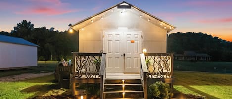 Une petite construction illuminée, dotée d’une porte et d’un escalier menant à l’entrée, et entourée d’un jardin.