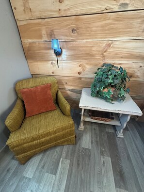 A room with a wooden wall, a small white table with a plant, and a gold-colored armchair with a red cushion. - Stylish Unique Cabin. Direct Access to Brimstone. Hot Tubs. Fire Pits. Pets Yes (Huntsville)