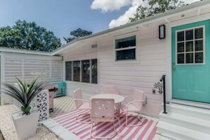 A patio with a table and chairs, a teal door, and a white exterior wall. - The Cabana on the Coast (Gulfport)