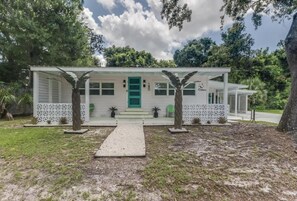 A single-story building with a covered porch, a green door, and a small front yard with two potted plants. - The Cabana on the Coast (Gulfport)