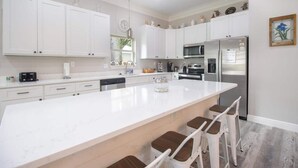 Una cocina moderna con armarios blancos, una isla grande, taburetes de bar y electrodomésticos de acero inoxidable.