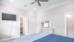 Un dormitorio con una cama, ventilador de techo, televisión, cómoda y espejo.