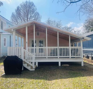 A single-story house with a covered porch, a staircase leading to the entrance, and a black object on the ground.