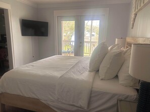 A bedroom with a bed, pillows, a TV, and a sliding glass door leading to an outdoor area.