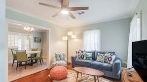 A living room with a sofa, ottoman, coffee table, and a ceiling fan. - The Little Sandy Flamingo (Gulfport)