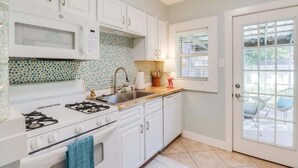 A kitchen with white cabinets, a stove, a sink, and a window with a view of outdoor furniture. - The Little Sandy Flamingo (Gulfport)