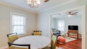 A dining area with a round table and chairs, a television, and a ceiling fan. - The Little Sandy Flamingo (Gulfport)