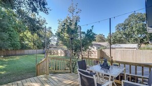 A wooden deck with a table and chairs, surrounded by a wooden fence and trees. - The Cozy Blue Cottage (Long Beach)