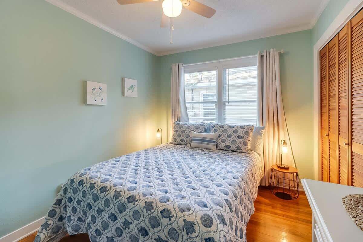 A bedroom with a bed, a ceiling fan, a window with curtains, and a bedside table with a lamp.