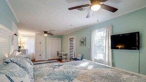 A bedroom with a bed, ceiling fan, TV, and a view of the hallway. - The Cozy Blue Cottage (Long Beach)