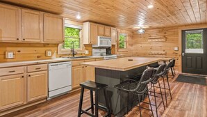 Cocina con paneles de madera, una isla central, taburetes de bar y lavavajillas.