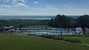 Vista de una piscina con valla, rodeada de césped y árboles, bajo un cielo parcialmente nublado.