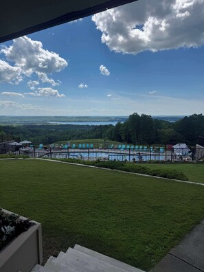 Blick auf einen Pool mit Zaun, umgeben von Gras und Bäumen, unter einem teilweise bewölkten Himmel.