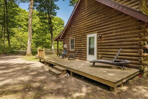 Eine Blockhütte mit einer Terrasse, zwei Stühlen und einer Liege.