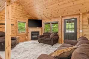 Ein Blockhaus-Interieur mit Kamin, Fernseher und zwei Sofas.