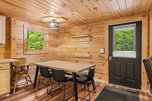 A wooden interior with a dining table, chairs, a black door, and a window with a view of greenery. - North Haven Lodge | Shanty Creek | Pets | Bellaire (Bellaire)