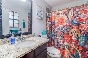 Ein Badezimmer mit einem großen Spiegel, einem Waschbecken mit Marmorplatte, einem Duschvorhang mit buntem Paisley-Muster und einer weißen Toilette.
