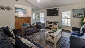 A living room with a sofa, armchairs, a coffee table, a TV, and artwork on the walls. - The Gulf Breeze Getaway (Gulfport)