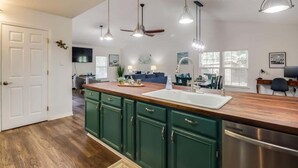 A kitchen with a wooden countertop, green cabinets, a stainless steel dishwasher, pendant lights, and a ceiling fan. - The Gulf Breeze Getaway (Gulfport)
